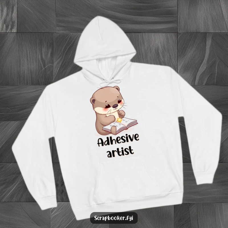 Funny hoodie depicting a cute otter in the act of gluing a shiny embellishment onto a craft page, offering warmth and humor.